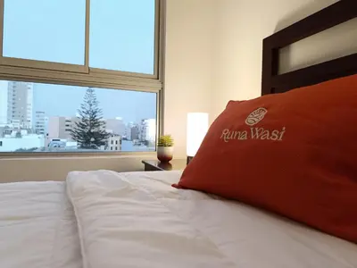 a bed with a red pillow in a room with a window at Runawasi Apartments - Amaru 3BDR in Lima