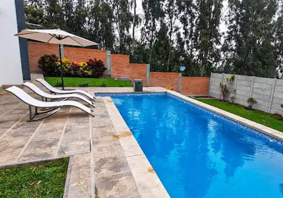 a swimming pool with two chairs and an umbrella at KUSI WASI CIENEGUILLA in Cieneguilla