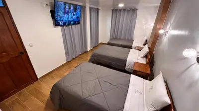 a small room with two beds and a flat screen tv at QUECHUA´S HOUSE Hostal & Coffee in Machu Picchu