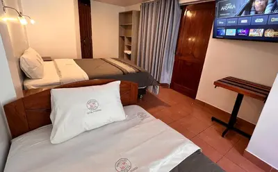 a room with two beds and a flat screen tv at QUECHUA´S HOUSE Hostal & Coffee in Machu Picchu