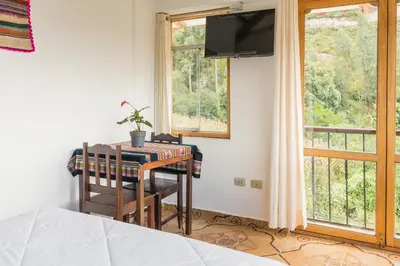 a bedroom with a desk and a balcony with a television at Sueños del Valle Sagrado in Urubamba