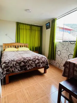 a bedroom with a bed with green curtains and a window at Euro Hostal in Cusco