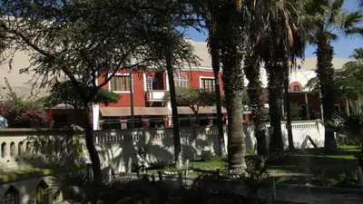 a red building with palm trees and a fence at Hostal Huacachina Sunset in Ica