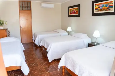 a hotel room with three beds with white sheets at Hotel Curasi in Ica