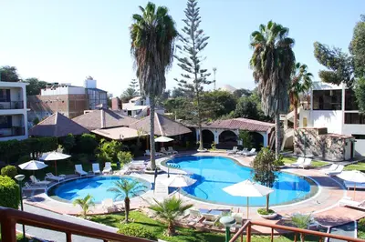 a resort pool with chairs and umbrellas and palm trees at Hotel Villa de Valverde in Ica