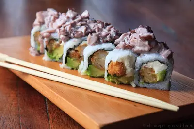 a group of sushi on a wooden plate with chopsticks at Hotel El Huarango in Ica