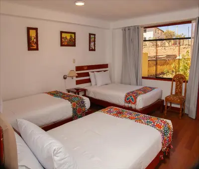 a hotel room with three beds and a window at Hotel Valle Mistico in Ollantaytambo