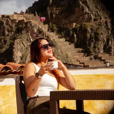 a woman sitting on a bench drinking a cup of coffee at Hotel Valle Mistico in Ollantaytambo
