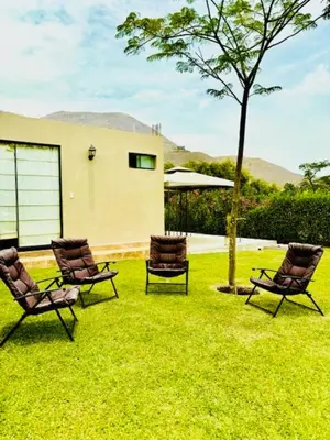 three chairs sitting in the grass in front of a house at Casa de Campo Bamboo con Piscina temperada in Lima