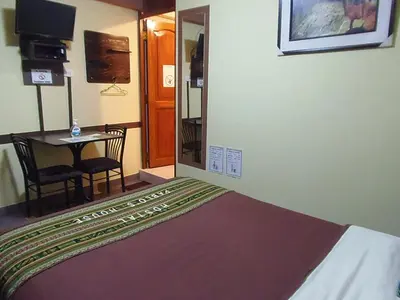 a room with a bed and a table and a mirror at Hostal Pablo's House in Machu Picchu