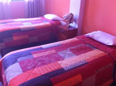 a bedroom with two beds and a table with a quilt at Hostal Tres Máscaras in Ayacucho