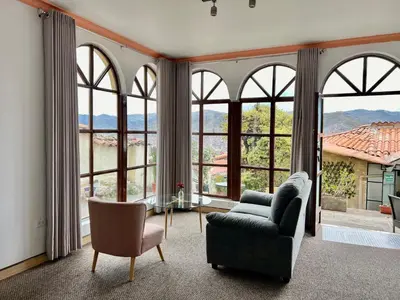 a living room with large windows and a couch and chair at Casa Encuentro San Blas in Cusco