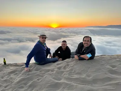 three men sitting on top of a sand hill with the sunset at Acari Adventure & ski Resort in Acarí