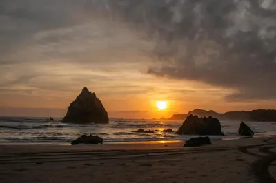 a sunset on a beach with rocks in the ocean at Acari Adventure & ski Resort in Acarí