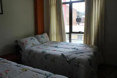 two beds in a room with a window at Hostal Inkanto Taruma in Tarma