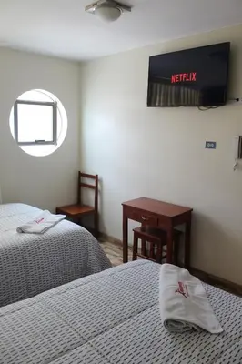 a room with two beds and a desk and a sign on the wall at Hostal Inkanto Taruma in Tarma