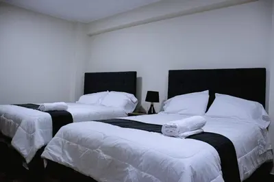 two beds in a bedroom with white sheets and pillows at PRANA in Huancayo