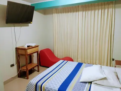 a bedroom with a bed and a red chair and a television at HOSTAL TOSCANO SUITES in El Tambo