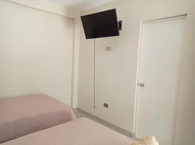a bedroom with two beds and a tv on the wall at Hotel Sunlight in Paracas