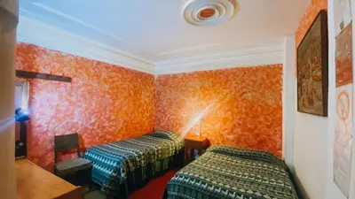 two beds in a room with orange wallpaper at Royal Frankenstein Hostel in Cusco