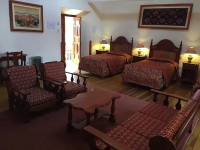 a room with three beds and chairs and a table at Hotel Midori in Cusco