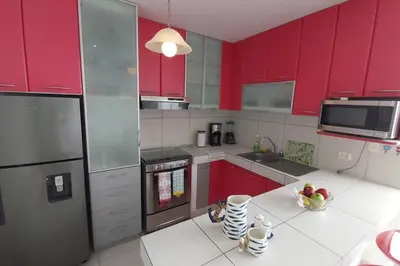 a kitchen with red cabinets and a white counter top at Departamento en playa Chocaya. Disfruta del mar, la piscina y la tranquilidad. in Asia