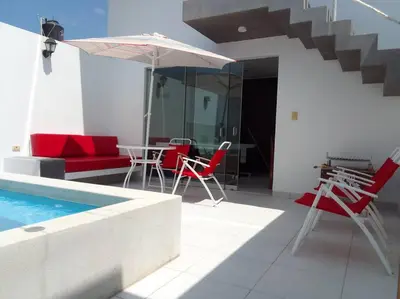a house with a pool and red chairs and an umbrella at Departamento en playa Chocaya. Disfruta del mar, la piscina y la tranquilidad. in Asia