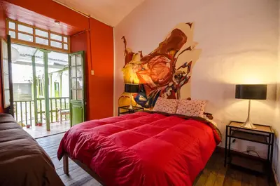 a bedroom with a red bed with a painting on the wall at Dragonfly Hostels Cusco in Cusco