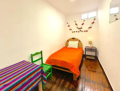 a bedroom with an orange bed and a table at Dragonfly Hostels Cusco in Cusco