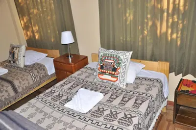 a bedroom with two beds and a table with a lamp at Hostal Goya Andina in Cusco