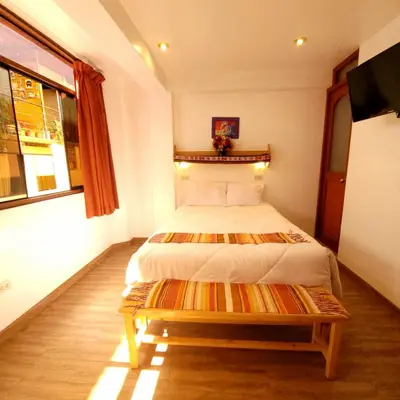 a bedroom with a bed and a bench in it at Hotel Ruta Amazónica Machupicchu in Machu Picchu