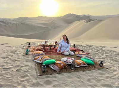 a woman sitting in the sand in the desert at dos apartamentos cerca de la laguna de Huacachina in Ica