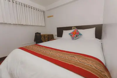 a bedroom with a white bed with a colorful pillow on it at Lucios Cusco in Cusco