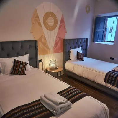 a room with two beds with a painting on the wall at Way Kap Hostel Cusco in Cusco