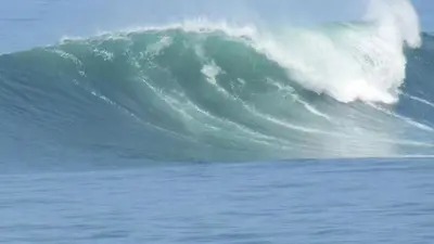 a large wave in the ocean with a surfer riding it at Punta Hermosa in Punta Hermosa