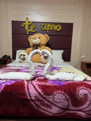 a teddy bear sitting on a bed with two swans at 100pre feliz in Lima