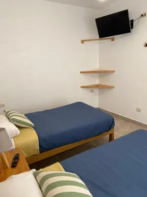a room with two beds and a flat screen tv at Ravenala Paracas Hostel & Apartment in Paracas