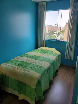 a bedroom with a bed in a blue room with a window at Edificio Parque Suarez - San Miguel in Lima