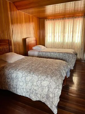 two beds in a bedroom with wooden walls and wood floors at DCampos Lodge in Oxapampa