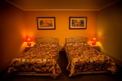 two beds in a room with orange walls and two lamps at Hotel Rivera in Ayacucho