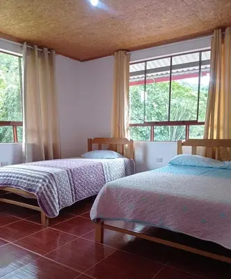 two beds in a room with two windows at Hospedaje Casablanca in Pozuzo