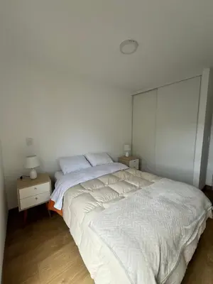 a bedroom with a large white bed and a night stand at Cómodo y Acogedor Departamento Cerca de Barranco y el Circuito de Playas in Lima