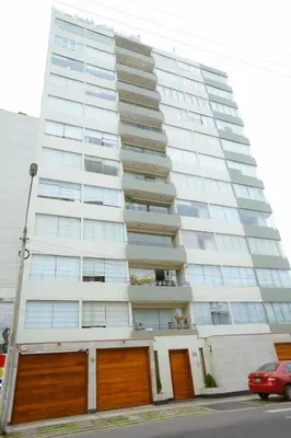 a tall white building with brown doors and a red car at Bello Familiar Miraflores Larcomar Kennedy in Lima
