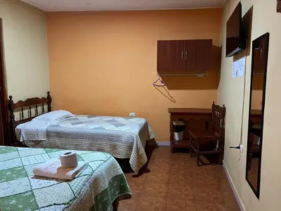 a room with two beds and a cabinet and a table at Hospedaje El Centro in Ayacucho