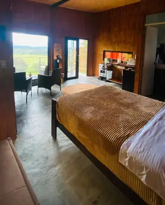 a bedroom with a large bed and a desk and a kitchen at Cabaña1 con hermosa vista al valle in Oxapampa