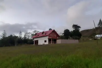 a house with a red roof in a field at Posada de la Sirga Oxapampa De 8 a 10 personas in Oxapampa
