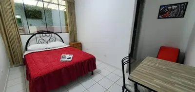 a small room with a bed with a red blanket and a table at Hospedaje El Paraiso in Santa Eulalia