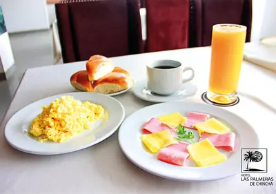 a table with two plates of food and a glass of orange juice at Qallwa Chincha in Chincha Alta