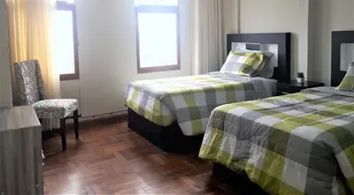 a bedroom with two beds and a chair and window at Royalty Inn in Lima
