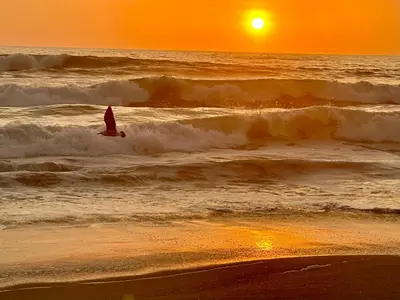 a person on a surfboard in the ocean at sunset at Refugio del Mar Wakama in San Vicente de Cañete